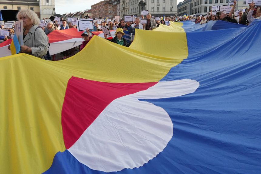 Tłum demonstrantów trzymających wielką flagę, z transparentami w dłoniach.