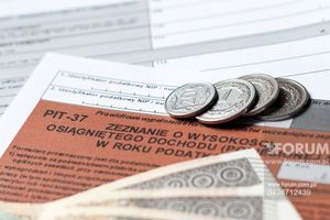 Opis ALT: Dokumenty podatkowe (PIT-37) z monetami oraz banknotami w tle.