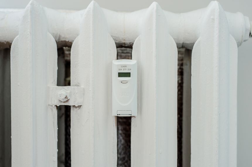Biały kaloryfer z elektronicznym licznikem zamontowanym na jego bocznej części.