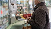 Osoba starsza w sklepie aptecznym rozmawia z farmaceutą za szybą. Trzyma czerwoną torebkę.