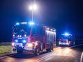 Na zdjęciu widoczne są dwa czerwone wozy strażackie z niebieskimi i białymi światłami na drodze nocą.