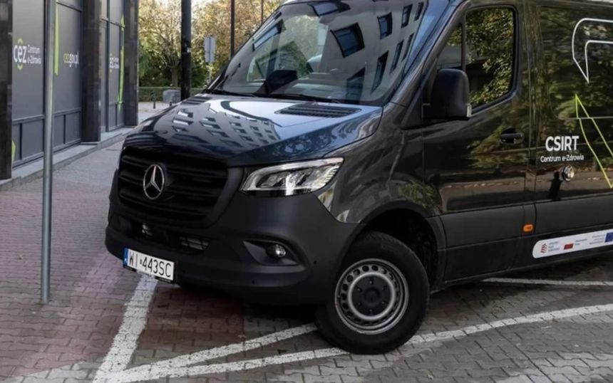Czarny samochód dostawczy zaparkowany w strefie zabronionej obok budynku.