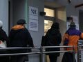 Na zdjęciu cztery osoby stojące w kolejce do budynku NFZ w chłodny dzień.