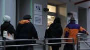 Na zdjęciu cztery osoby stojące w kolejce do budynku NFZ w chłodny dzień.