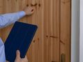 Mężczyzna w jasnej koszuli puka do drewnianych drzwi, trzymając niebieską tabletkę.