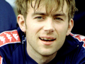 Damon Albarn z zespołu Blur. Mężczyzna z krótkimi włosami, uśmiechający się w sportowym stroju, siedzi na ławce.