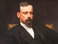 Portret mężczyzny w eleganckim stroju, z poważnym wyrazem twarzy, siedzącego na krześle.