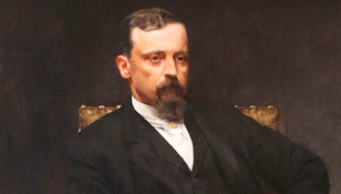 Portret mężczyzny w eleganckim stroju, z poważnym wyrazem twarzy, siedzącego na krześle.