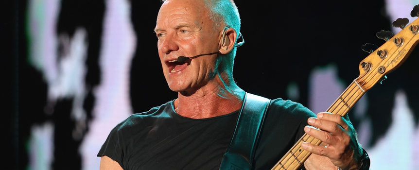 Mężczyzna w czarnym t-shircie gra na gitarze basowej i śpiewa na scenie.