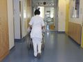 Na zdjęciu widoczna jest pielęgniarka prowadząca wózek inwalidzki w szpitalnym korytarzu.
