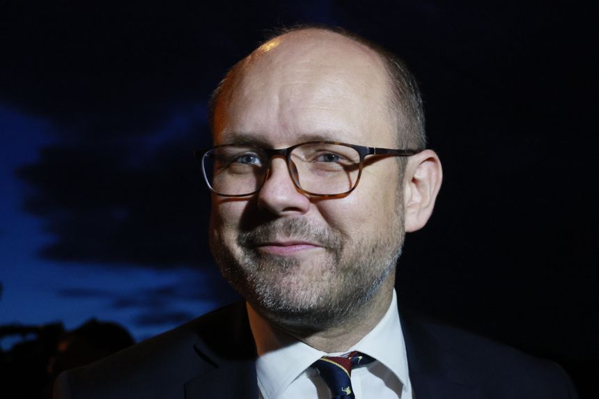 Mężczyzna w okularach, z uśmiechem, w garniturze, na tle ciemnego nieba.