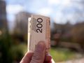 Zbliżenie na banknot 200 złotych trzymany w dłoni, w tle rozmyty krajobraz.