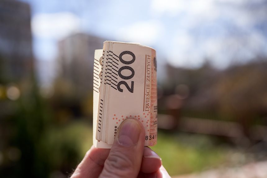 Zbliżenie na banknot 200 złotych trzymany w dłoni, w tle rozmyty krajobraz.
