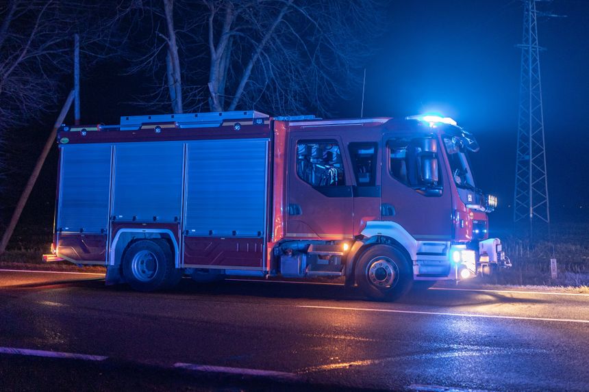 Czerwony wóz strażacki z niebieskimi sygnalizatorami na drodze w nocy.