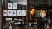Witryna restauracji z napisami „NA WYNOS”, „PIZZA”, „BURGER”, „STEK”, „SHOARMA”.