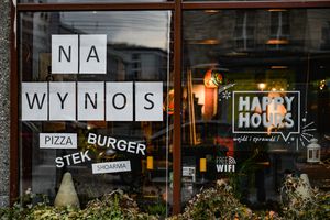 Witryna restauracji z napisami „NA WYNOS”, „PIZZA”, „BURGER”, „STEK”, „SHOARMA”.