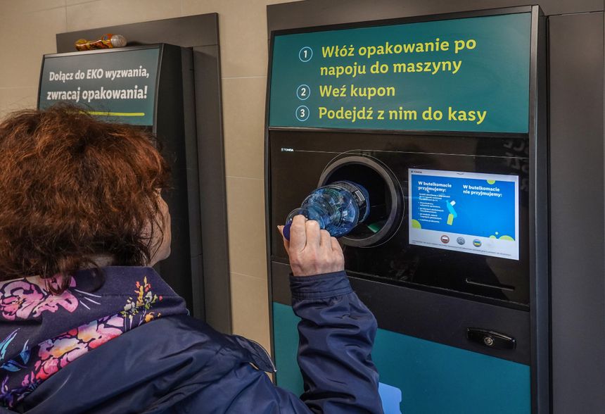 Osoba wrzucająca plastikową butelkę do automatu do zwrotu opakowań. Informacje o procesie na ekranie.