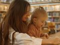 Matka z dzieckiem w bibliotece, angażują się w czytanie i naukę, otoczeni półkami z książkami.