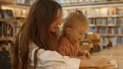 Matka z dzieckiem w bibliotece, angażują się w czytanie i naukę, otoczeni półkami z książkami.