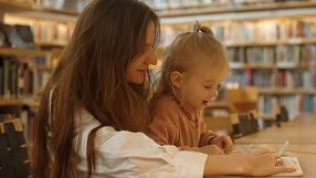 Matka z dzieckiem w bibliotece, angażują się w czytanie i naukę, otoczeni półkami z książkami.
