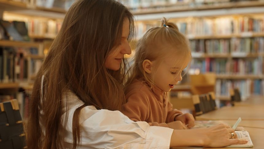 Matka z dzieckiem w bibliotece, angażują się w czytanie i naukę, otoczeni półkami z książkami.