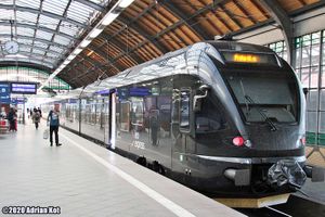 Pociąg Leo Express na stacji, przy peronie z pasażerem i dużymi oknami.