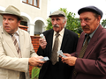 Trzej mężczyźni w garniturach, wymieniają pieniądze pod dużym budynkiem.
