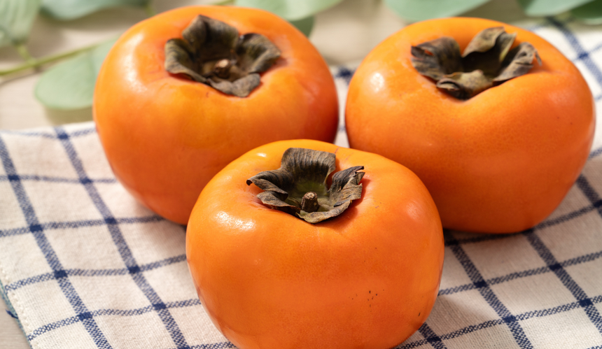 Trzy persymony (kaki) na ręczniku kuchennym w kratkę