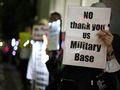 Protestujący trzymają transparent „NO thank you US Military Base” w tłumie.