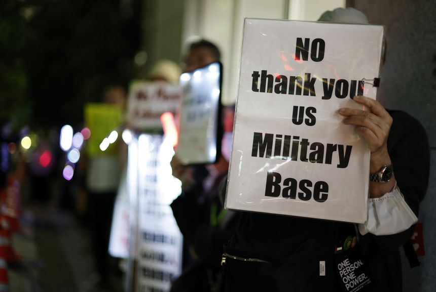 Protestujący trzymają transparent „NO thank you US Military Base” w tłumie.