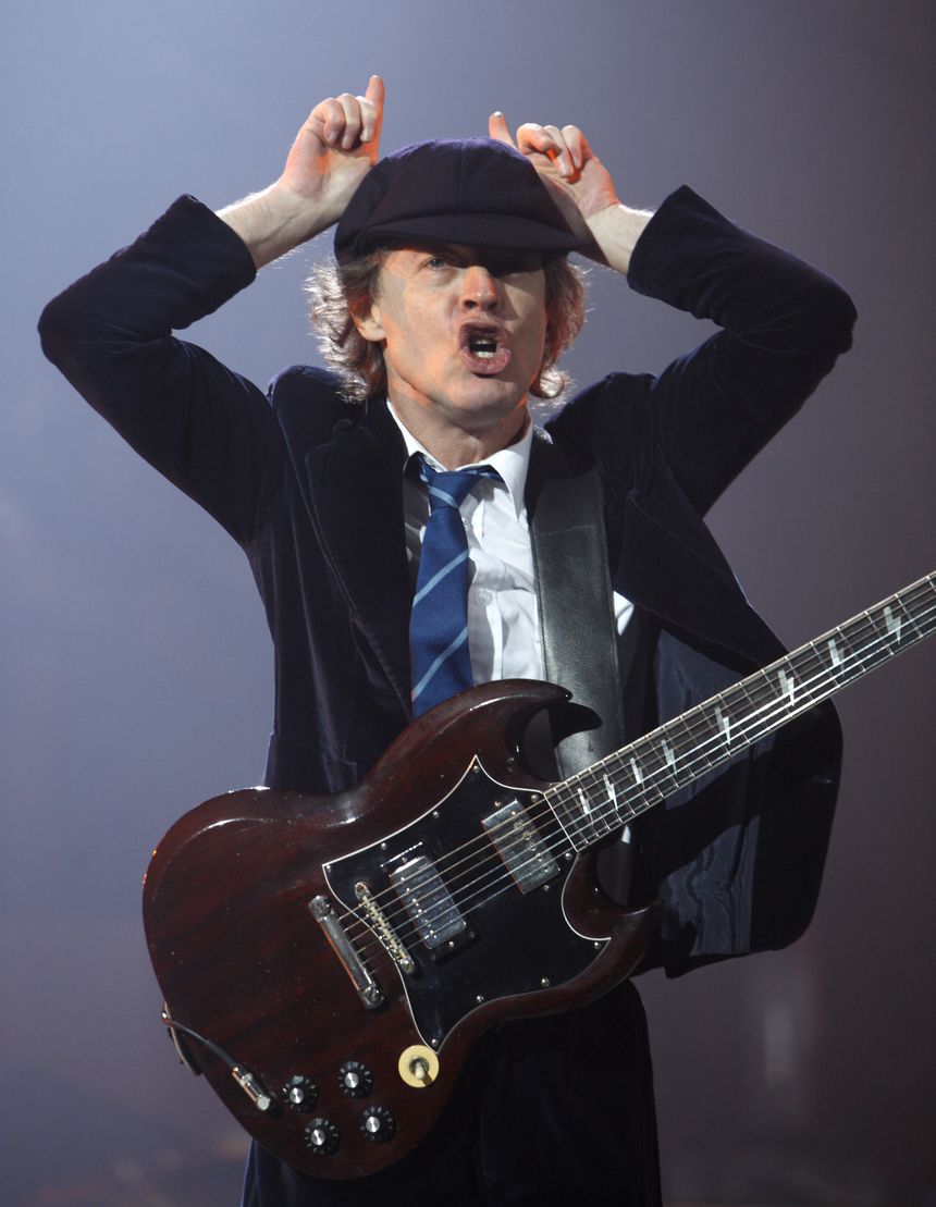 Mężczyzna grający na gitarze elektrycznej, z wyrazem entuzjazmu i kapeluszem na głowie.
