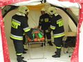Czterech strażaków w mundurach ratunkowych transportuje poszkodowanego na noszach w namiocie.