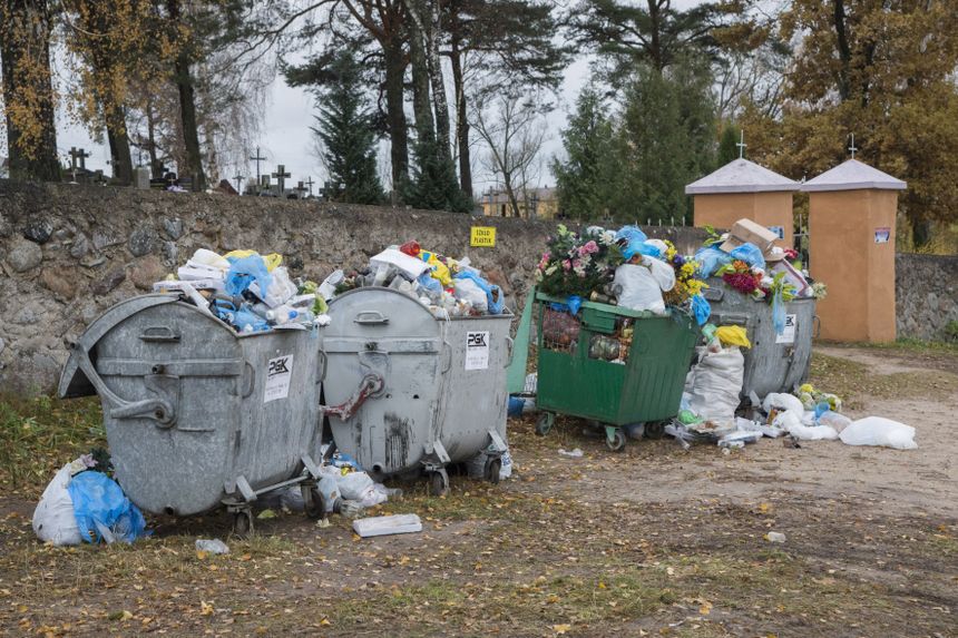 Śmietniki przepełnione odpadami w otoczeniu cmentarza. Jesień, liście na ziemi.