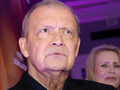 Mężczyzna zrzuca poważne spojrzenie, w tle widoczna kobieta i delikatne światło.