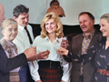 Grupa sześciu osób w radosnej atmosferze, wznoszących szkło, w stylowych ubraniach.