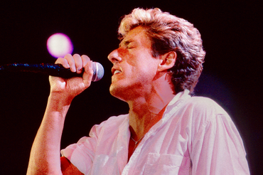 Roger Daltrey z The Who. Mężczyzna z mikrofonem śpiewa, zamknięte oczy, intensywne oświetlenie w tle.
