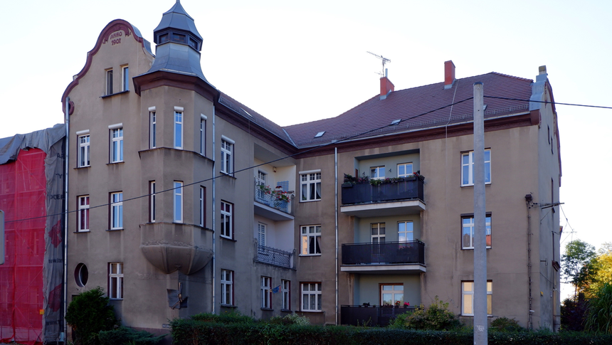 Budynki mieszkalne z balkonami, styl architektoniczny z początku XX wieku, otoczone zielenią.