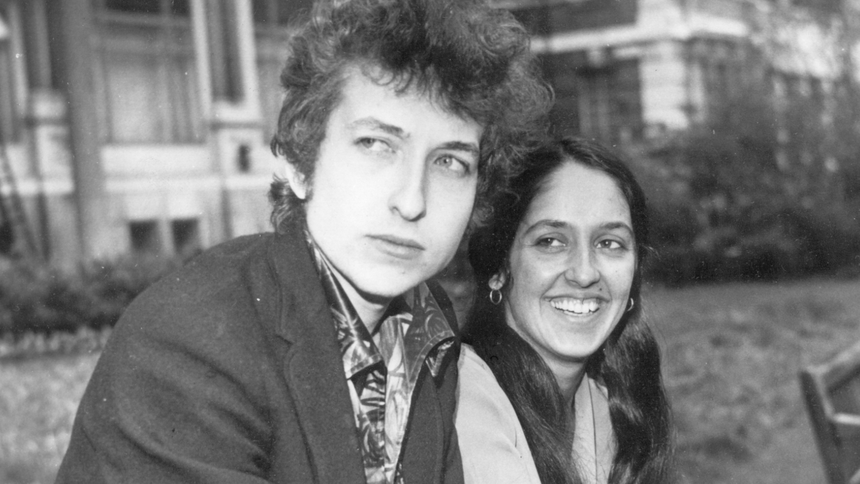 Bob Dylan i Joan Baez w 1965 roku. Młody mężczyzna z kręconymi włosami i uśmiechnięta kobieta na tle budynków.
