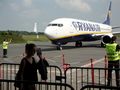 Samolot Ryanair na płycie lotniska, w tle osoby w kamizelkach ostrzegawczych.