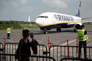 Samolot Ryanair na płycie lotniska, w tle osoby w kamizelkach ostrzegawczych.