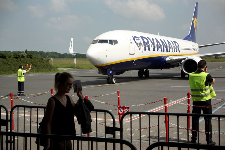 Samolot Ryanair na płycie lotniska, w tle osoby w kamizelkach ostrzegawczych.