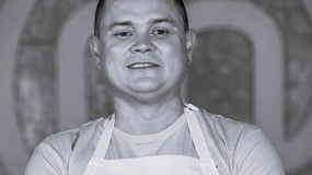 Mariusz Komenda w jasnej koszulce i fartuchu kuchennym, uśmiechnięty, w tle rozmyte kształty.