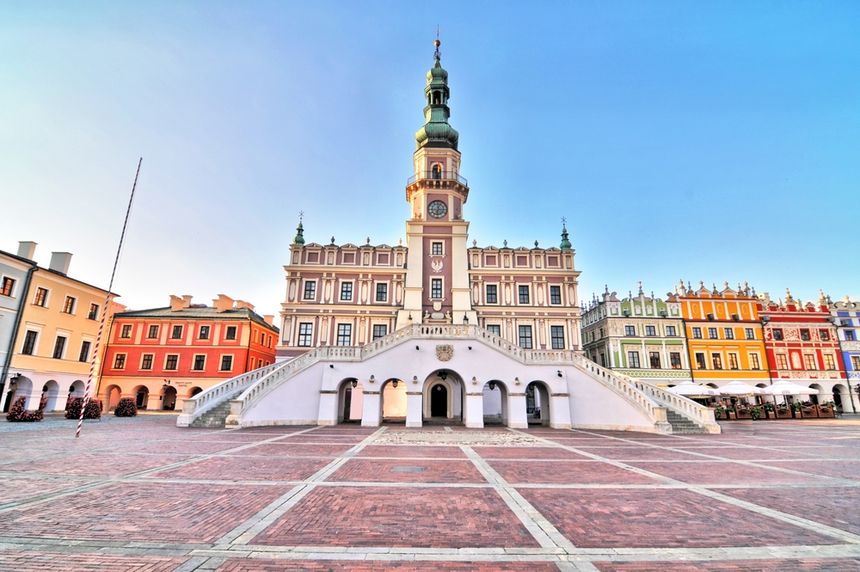 Zabytkowy ratusz w Zamościu z kolorowymi kamienicami na tle błękitnego nieba.