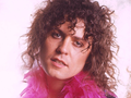 Marc Bolan w 1970 roku. Mężczyzna z kręconymi włosami, w różowym boa, patrzy w stronę obiektywu. Tło zamglone.