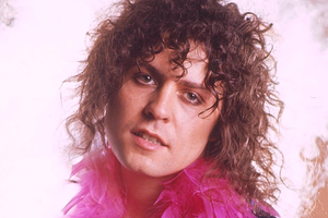 Marc Bolan w 1970 roku. Mężczyzna z kręconymi włosami, w różowym boa, patrzy w stronę obiektywu. Tło zamglone.