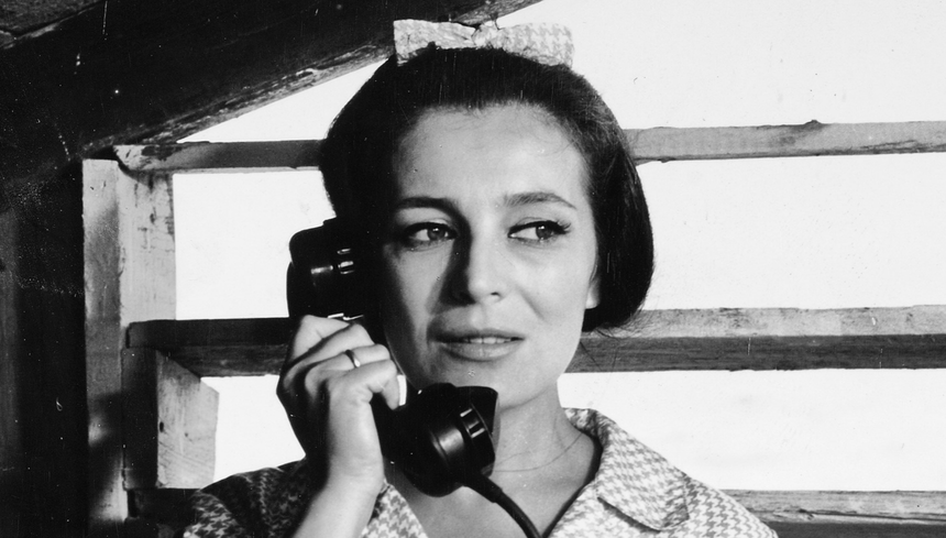 Kobieta z telefonem, w retro stylizacji, rozmawia z kimś, w tle drewniane elementy konstrukcyjne.