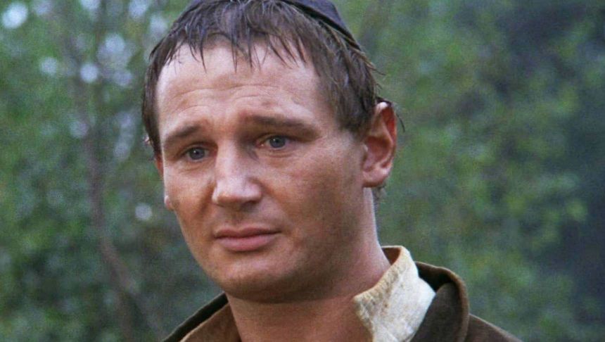 Mężczyzna z krótkimi, ciemnymi włosami, wyraz twarzy zmartwiony, w tle zieleń drzew.