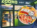 Zielony sklep Żabka, z logo nad wejściem, i obrazek pizzy Fat Peppa w okrągłym ramku.
