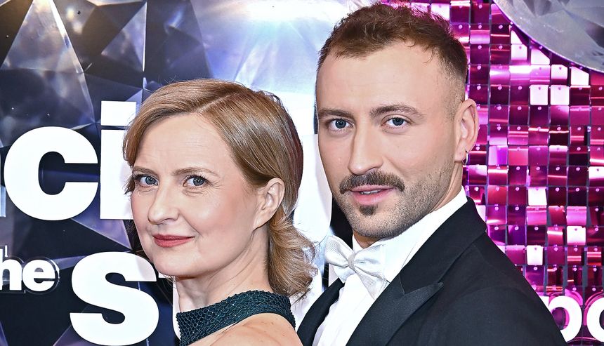 Izabela Kuna na tle błyszczącego tła z napisem 