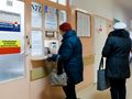 Na zdjęciu dwie kobiety w kurtkach stoją przy oknie rejestracyjnym w przychodni.
